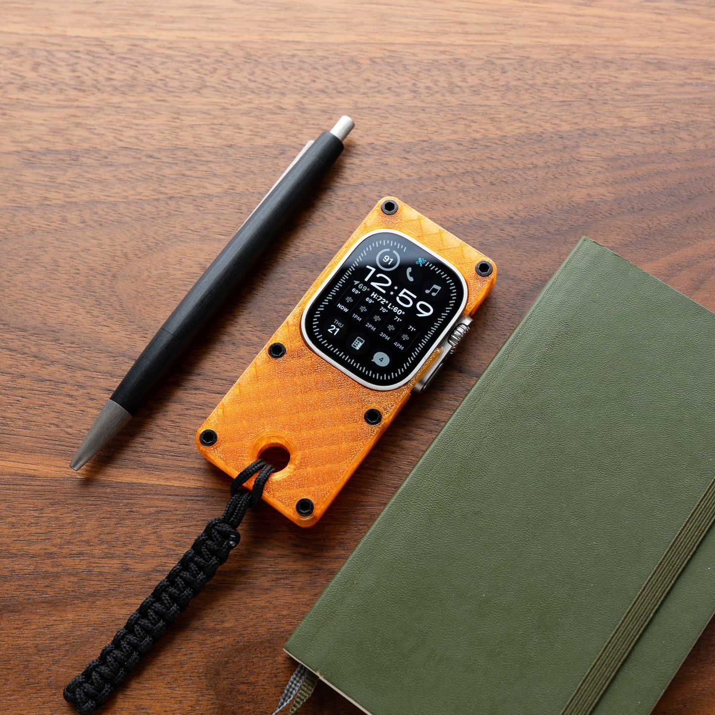 miniphone ultra orange Apple Watch Ultra case flat lay on wood desk beside pen and notebook